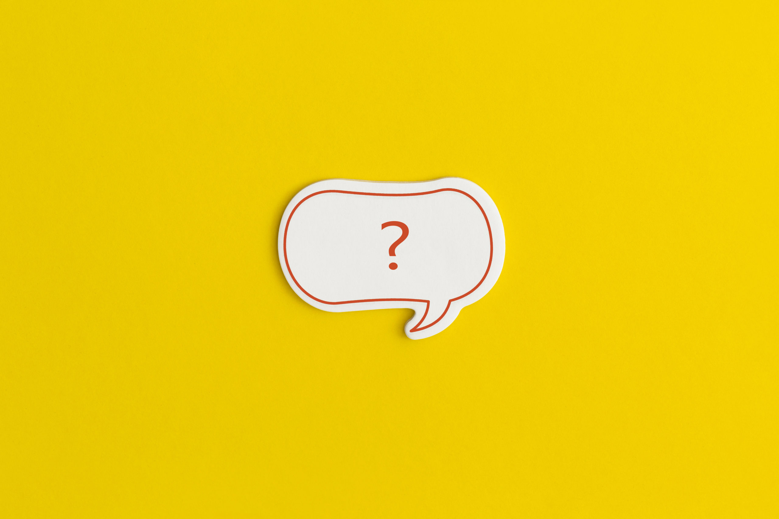 Paper speech bubble on a yellow background. Question mark