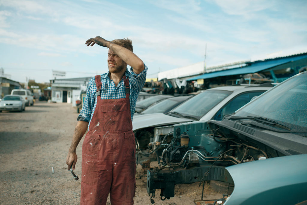 Tired repairman with wrench on car junkyard